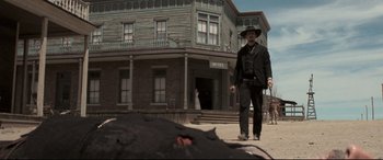 Movie still from “In a Valley of Violence” (2016), directed by Ti West – A man in a black suit and a black hat walking in front of a building; Wide shot, Low angle