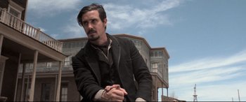 Movie still from “In a Valley of Violence” (2016), directed by Ti West – A man with a beard and mustache wearing a black jacket; Medium shot, Low angle