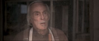 Movie still from “In a Valley of Violence” (2016), directed by Ti West – An old man wearing an apron looking out of a window; Close Up shot, Over the shoulder angle