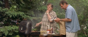Movie still from “In the Bedroom” (2001), directed by Todd Field – A man standing next to another man cooking food on a grill; Medium shot, Low angle