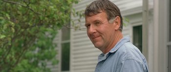 Movie still from “In the Bedroom” (2001), directed by Todd Field – A person wearing a blue shirt near a building; Close Up shot, Over the shoulder angle