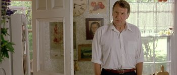 Movie still from “In the Bedroom” (2001), directed by Todd Field – A man standing in front of a wall with pictures on the wall; Medium shot, Over the shoulder angle