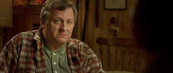Movie still from “In the Bedroom” (2001), directed by Todd Field – An older man sitting in front of a wooden wall; Close Up shot, Over the shoulder angle