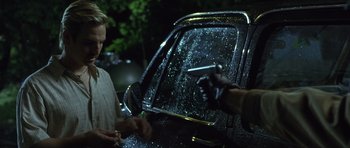 Movie still from “In the Bedroom” (2001), directed by Todd Field – A man holding a cell phone in front of a parked car; Medium shot, Over the shoulder angle