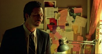 Movie still from “In the Cut” (2003), directed by Jane Campion – A man wearing a suit and tie in front of a wall covered with papers; Close Up shot, Low angle