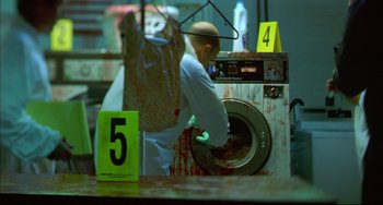Movie still from “In the Cut” (2003), directed by Jane Campion – A man in a white lab coat is washing clothes in a washing machine; Wide shot, High angle