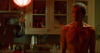 Movie still from “In the Cut” (2003), directed by Jane Campion – A man standing in a kitchen next to a lamp; Medium shot, Over the shoulder angle