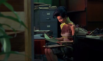 Movie still from “In the Mood for Love” (2000), directed by Kar-Wai Wong – A woman sitting at a desk looking at a piece of paper; Medium shot, High angle