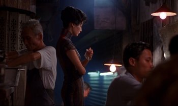 Movie still from “In the Mood for Love” (2000), directed by Kar-Wai Wong – A woman standing in front of a group of people; Medium shot, Over the shoulder angle