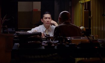 Movie still from “In the Mood for Love” (2000), directed by Kar-Wai Wong – A man sitting at a table talking to another man; Medium shot, Over the shoulder angle