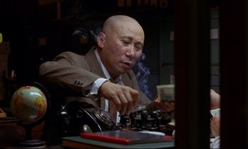 Movie still from “In the Mood for Love” (2000), directed by Kar-Wai Wong – An older man sitting in front of a typewriter holding money; Medium shot, Low angle