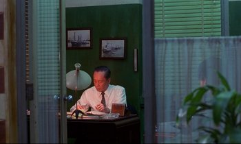 Movie still from “In the Mood for Love” (2000), directed by Kar-Wai Wong – A man sitting at a desk in front of a window; Medium shot, Low angle