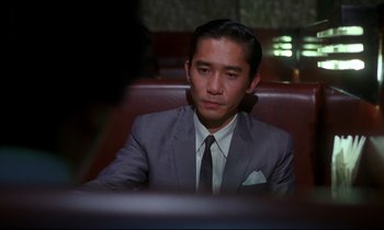 Movie still from “In the Mood for Love” (2000), directed by Kar-Wai Wong – A man in a suit and tie sitting at a table; Close Up shot, Over the shoulder angle