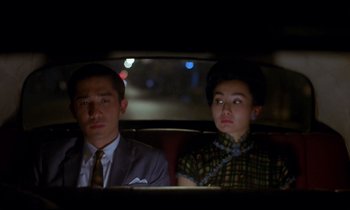 Movie still from “In the Mood for Love” (2000), directed by Kar-Wai Wong – A man and a woman sitting in the back of a car; Medium shot, Over the shoulder angle