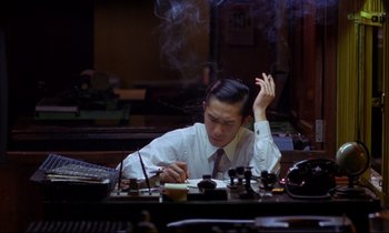 Movie still from “In the Mood for Love” (2000), directed by Kar-Wai Wong – A man sitting in front of a table with a cup of coffee; Medium shot, High angle