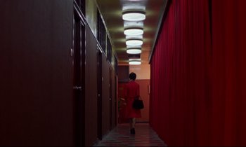 Movie still from “In the Mood for Love” (2000), directed by Kar-Wai Wong – A woman in a red dress walking down a long hallway; Extreme Wide shot, High angle