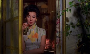 Movie still from “In the Mood for Love” (2000), directed by Kar-Wai Wong – A woman holding a drink in her hand and looking at the camera; Medium shot, Over the shoulder angle