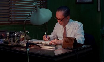 Movie still from “In the Mood for Love” (2000), directed by Kar-Wai Wong – An older man sitting at a desk writing on a piece of paper; Medium shot, Low angle