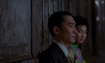 Movie still from “In the Mood for Love” (2000), directed by Kar-Wai Wong – A man and a woman standing next to each other in front of a wooden wall; Medium shot, Low angle