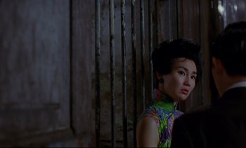Movie still from “In the Mood for Love” (2000), directed by Kar-Wai Wong – A woman in a floral dress standing in front of a metal fence; Close Up shot, Over the shoulder angle