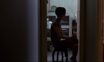 Movie still from “In the Mood for Love” (2000), directed by Kar-Wai Wong – A woman sitting on a stool in a room; Medium shot, Over the shoulder angle