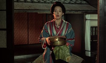 Movie still from “In the Realm of the Senses” (1976), directed by Nagisa Ôshima – A woman holding a bowl while standing in a room; Medium shot, High angle