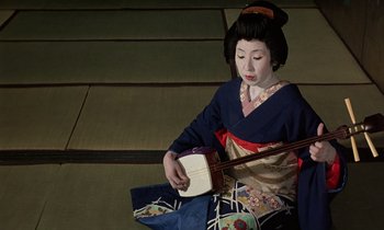 Movie still from “In the Realm of the Senses” (1976), directed by Nagisa Ôshima – A geisha playing a stringed musical instrument; Medium shot, High angle