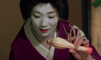 Movie still from “In the Realm of the Senses” (1976), directed by Nagisa Ôshima – A geisha is holding a piece of food in front of her face; Close Up shot, High angle