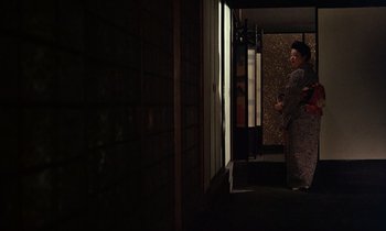 Movie still from “In the Realm of the Senses” (1976), directed by Nagisa Ôshima – A person standing in front of a window in the dark; Wide shot, Low angle