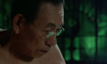 Movie still from “In the Realm of the Senses” (1976), directed by Nagisa Ôshima – An older man wearing glasses looking down at the ground; Close Up shot, High angle