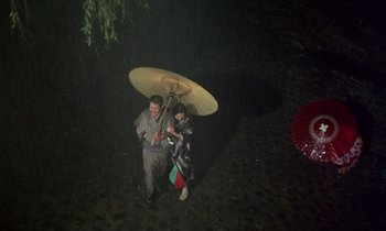 Movie still from “In the Realm of the Senses” (1976), directed by Nagisa Ôshima – A man and a woman standing under an umbrella; Extreme Wide shot, Overhead angle