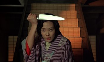 Movie still from “In the Realm of the Senses” (1976), directed by Nagisa Ôshima – A woman holding a large knife above her head; Medium shot, Low angle