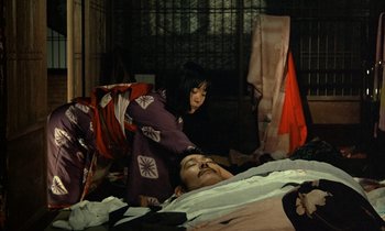 Movie still from “In the Realm of the Senses” (1976), directed by Nagisa Ôshima – A woman standing next to a man laying on a bed; Wide shot, High angle