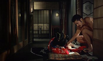 Movie still from “In the Realm of the Senses” (1976), directed by Nagisa Ôshima – A man sitting on the floor next to a bag of luggage; Wide shot, High angle