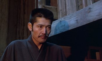 Movie still from “In the Realm of the Senses” (1976), directed by Nagisa Ôshima – A man in a black robe is standing in front of a wooden wall; Close Up shot, Low angle