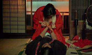 A woman in a red robe is tying a man's foot