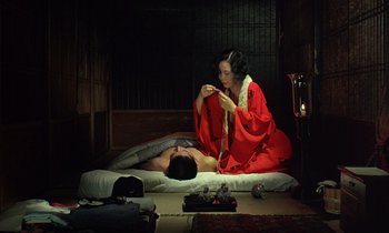 Movie still from “In the Realm of the Senses” (1976), directed by Nagisa Ôshima – A woman in a red kimono sitting next to a man in a red kimono; Medium shot, High angle