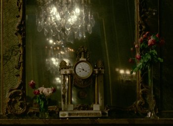 Movie still from “India Song” (1975), directed by Marguerite Duras – A clock sitting on top of a table in front of a mirror; Medium shot, High angle