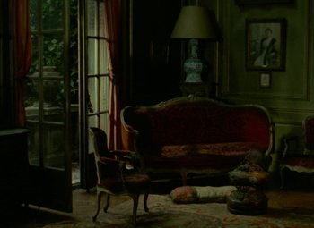 Movie still from “India Song” (1975), directed by Marguerite Duras – A living room filled with furniture next to an open door; Wide shot, High angle