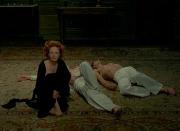 Movie still from “India Song” (1975), directed by Marguerite Duras – A woman sitting on the ground next to a man laying on the ground; Wide shot, High angle