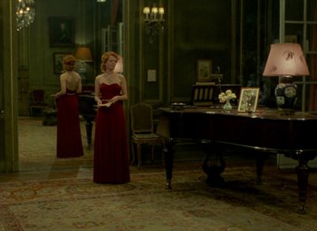 Movie still from “India Song” (1975), directed by Marguerite Duras – A woman in a red dress standing in front of a piano; Wide shot, Over the shoulder angle