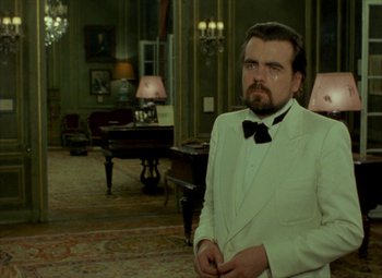 Movie still from “India Song” (1975), directed by Marguerite Duras – A man wearing a white suit and a black bow tie; Medium shot, Over the shoulder angle