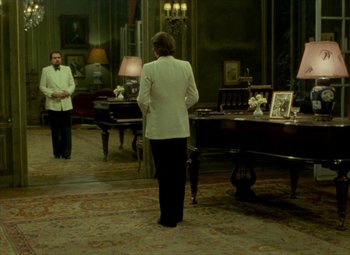 Movie still from “India Song” (1975), directed by Marguerite Duras – A man standing in front of a mirror in a room; Wide shot, High angle