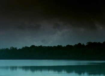 Movie still from “India Song” (1975), directed by Marguerite Duras – A body of water near a forest under a cloudy sky; Extreme Wide shot, High angle