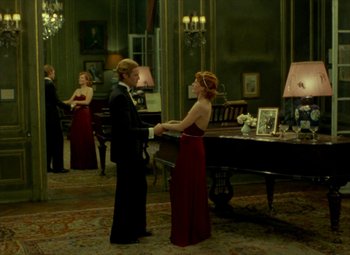 Movie still from “India Song” (1975), directed by Marguerite Duras – Two people in formal wear standing in front of a piano; Wide shot, High angle