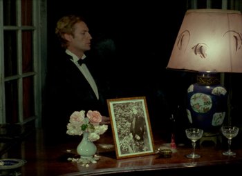Movie still from “India Song” (1975), directed by Marguerite Duras – A man sitting at a table in front of a picture; Medium shot, High angle
