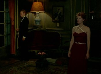 Movie still from “India Song” (1975), directed by Marguerite Duras – A man and a woman standing in front of a couch; Wide shot, High angle