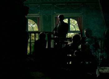 Movie still from “India Song” (1975), directed by Marguerite Duras – A group of people sitting in a room with a man in a suit; Wide shot, Low angle