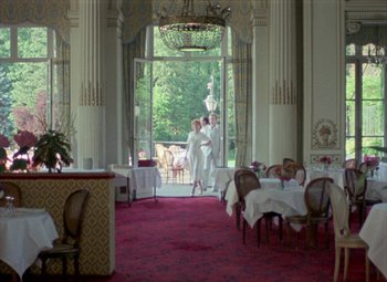 Movie still from “India Song” (1975), directed by Marguerite Duras – Two men in white shirts are standing in a restaurant; Extreme Wide shot, Low angle