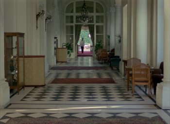 Movie still from “India Song” (1975), directed by Marguerite Duras – A person walking down a hall way in a building; Extreme Wide shot, High angle